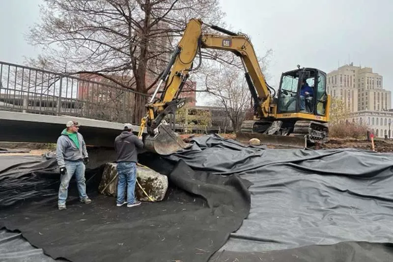 An outdoor commercial space with unfinished landscaping.  Employees of Knob Hill Landscape Company begin work on new landscaping.