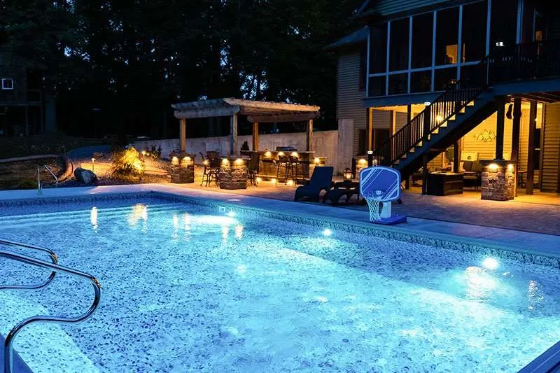 A large modern home with backyard landscaping, a patio, and inground pool at night designed by Knob Hill Landscaping Company of Springfield, Illinois. 
