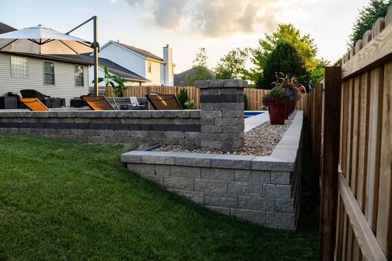 A fence lined with flowering landscaping, small rocks, and a concrete patio. Space designed by Knob Hill Landscape Company in Springfield, Illinois. 