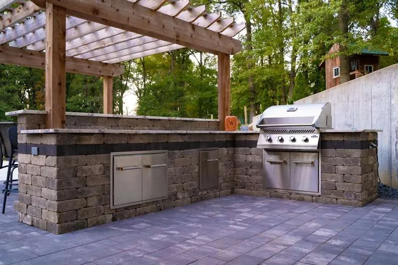 Backyard patio with built in countertops and grill with a pergola visible in the background. Space designed by Knob Hill Landscape Company of Springfield, Illinois. 