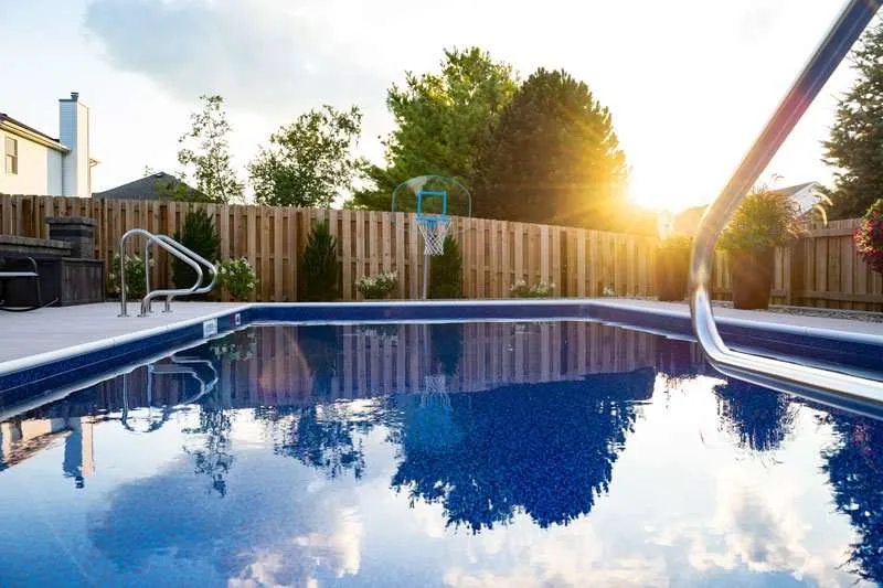 A modern residential patio space in a backyard with a large inground pool and flowering landscaping lining a fence. Space designed by Knob Hill Landscape Company of Springfield, Illinois. 