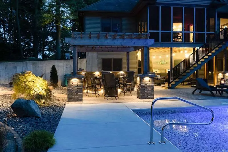 A large modern home with backyard landscaping, a patio, and inground pool at night designed by Knob Hill Landscaping Company of Springfield, Illinois. 