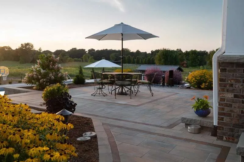 A large patio space for a modern residential home with seating, concrete patio pavers, and flowering plants designed by Knob Hill Landscape Company in Springfield, Illinois.