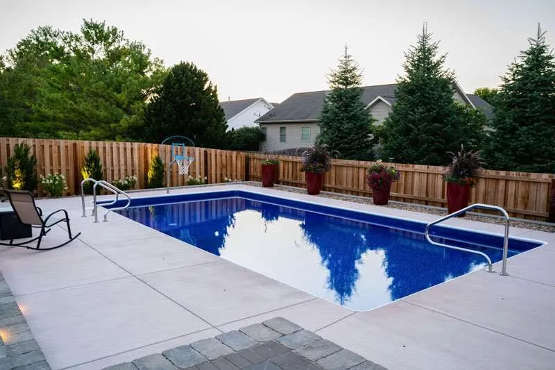 A modern residential patio space in a backyard with a large inground pool and flowering landscaping lining a fence. Space designed by Knob Hill Landscape Company of Springfield, Illinois. 