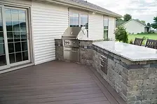 Patio on the back of a modern home with a stone retaining wall and inlaid grill and countertop designed by Knob Hill Landscape Company of Springfield, Illinois. 
