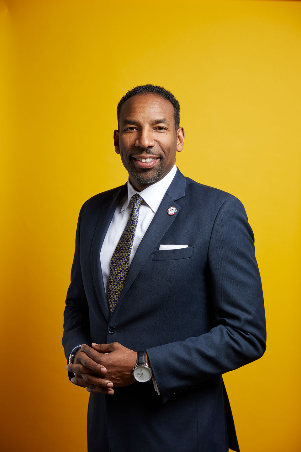 Portrait of Atlanta Mayor Andre Dickens in a blue suit and tie, smiling, with a yellow background
