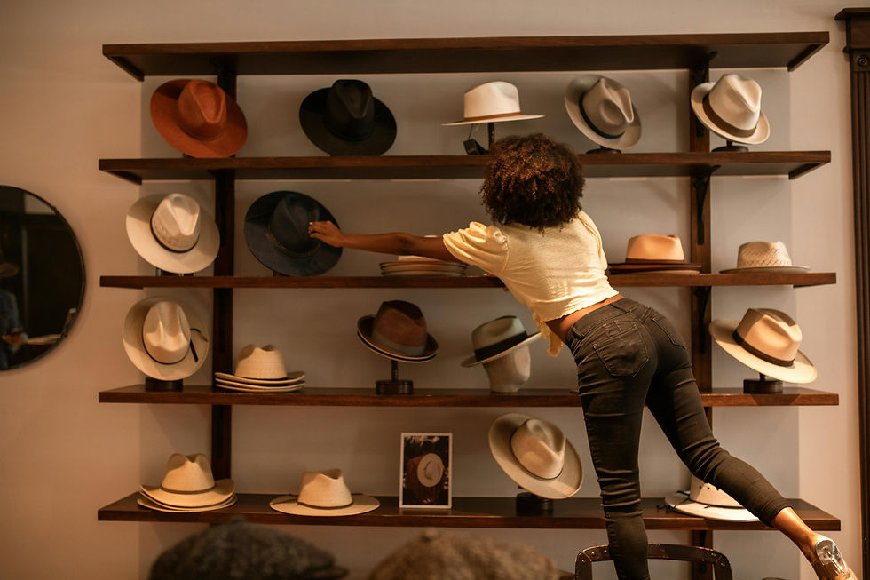 Woman on a stool adjusts hats on wooden shelves in a warm-lit boutique display