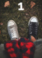Top-down view of two sneakers on grass with fallen leaves.