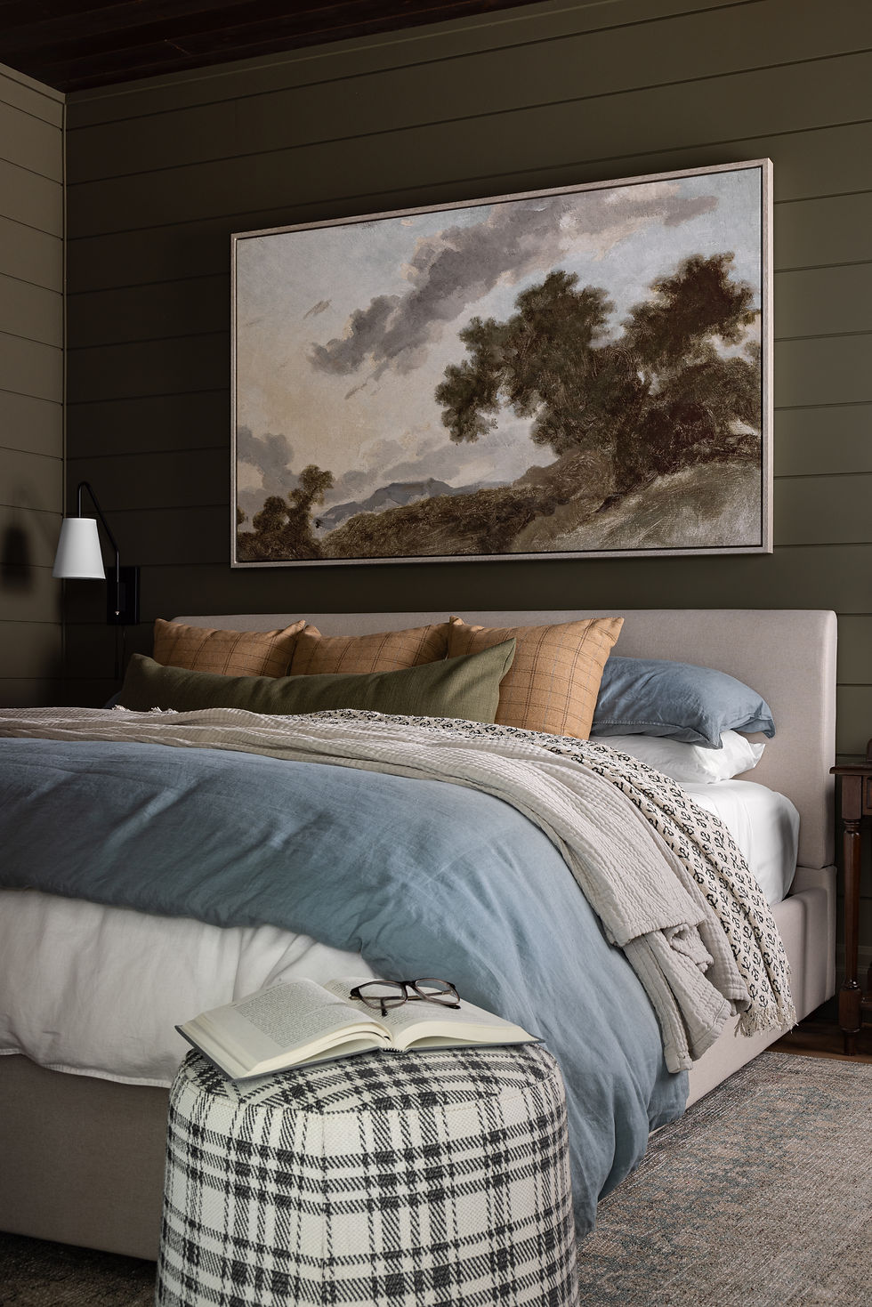 Cozy bedroom with layered bedding, blue throw, and large landscape artwork above the headboard