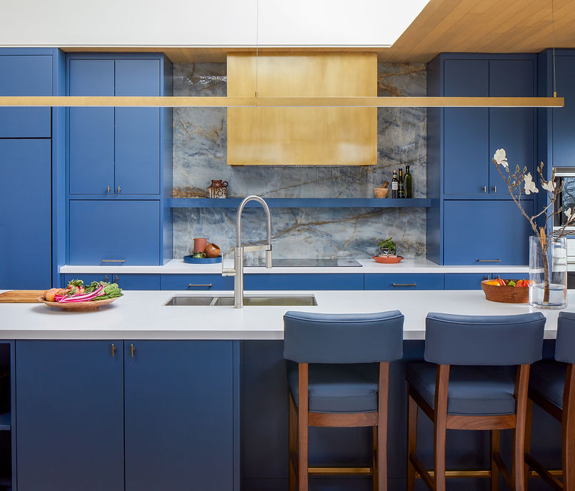 Blue lakeside kitchen with a white island, marble backsplash, brass range hood and large skylight