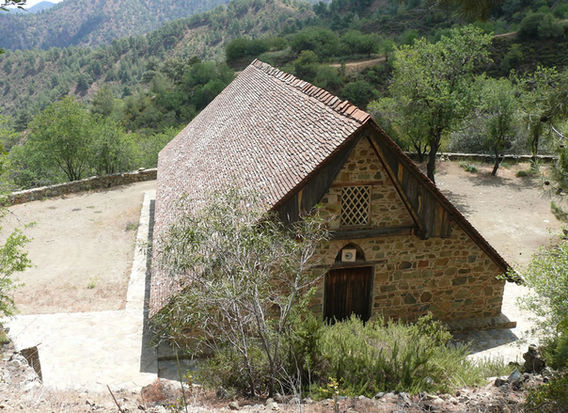 Close and downhill is tile roofed medieval Panagia tou Araka church. Many trees behind it.