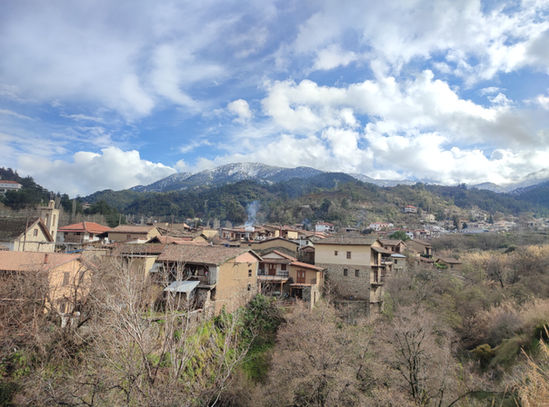 Winter photo of picturesque tile-roofed old part of Kakopetria village. Leafless alder trees in the foreground. Forested Troodos mountains in the background.