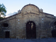 Famagusta Gate, on the medieval walls, from inside Nicosia. Front view of the gate arch and the big sandstone room around it. Two shorter walls and two oval windows and a stone arch above it. Clear sky.