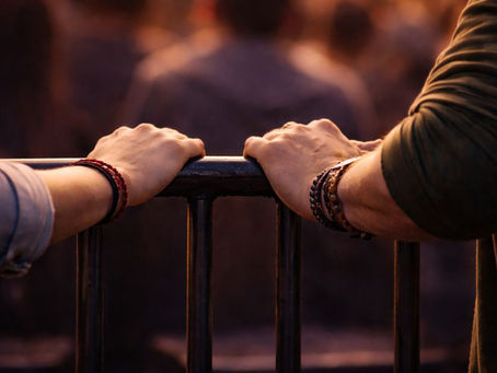 A lady's and a man's hand holding on to a bar their pinkies almost touching.