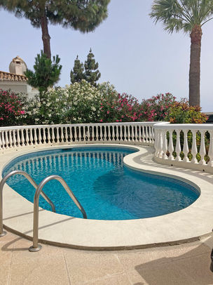 Curved outdoor pool with steps, white railing, and greenery