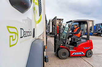 Worker operating a red forklift next to a Darcica truck.