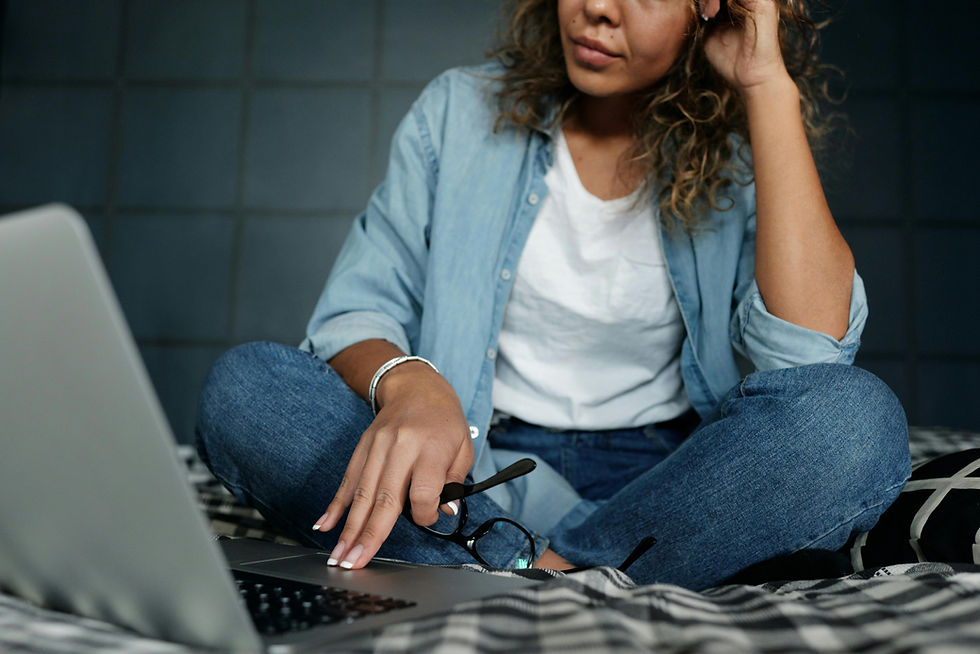 Casual woman working remotely on a laptop, sitting on a bed at home, focusing on the screen