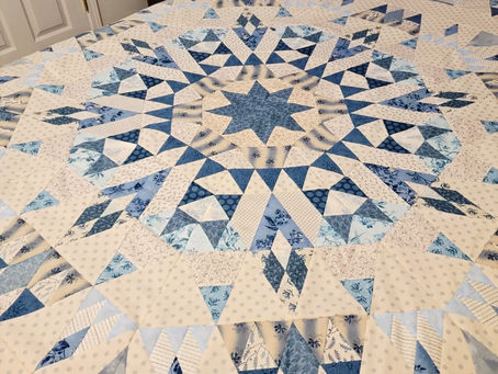 Blue-and-cream patchwork quilt with a starburst pattern spread across a bed in a bedroom, neat and decorative