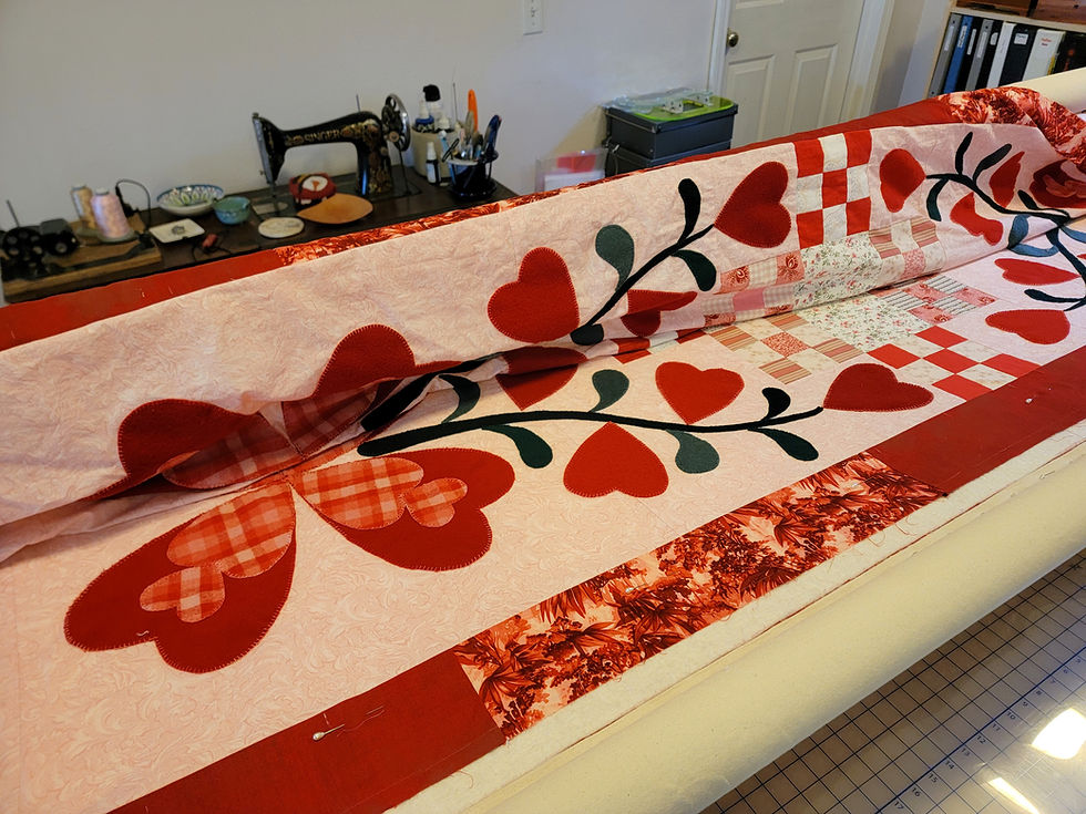 Heart-patterned quilt laid on a sewing table in a craft room, with a vintage sewing machine and tools in the background.