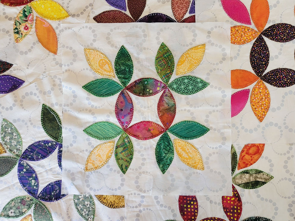 Colorful quilt blocks with stitched leaf-shaped fabric petals in pink, green, yellow, orange, and purple on a pale patterned background