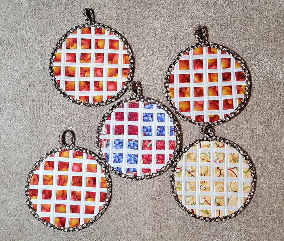 Five round quilted pot holders with fruit print patches on a beige textured surface, arranged in a cluster.