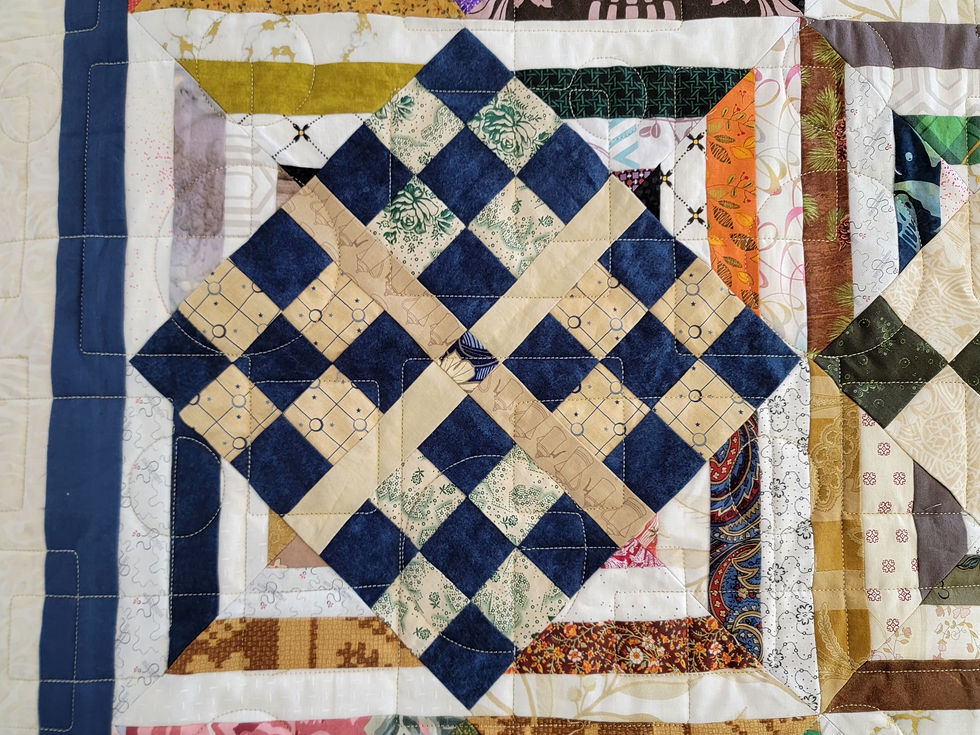 Close-up of a colorful patchwork quilt with navy, cream, and floral patterned squares stitched in a geometric diamond design.