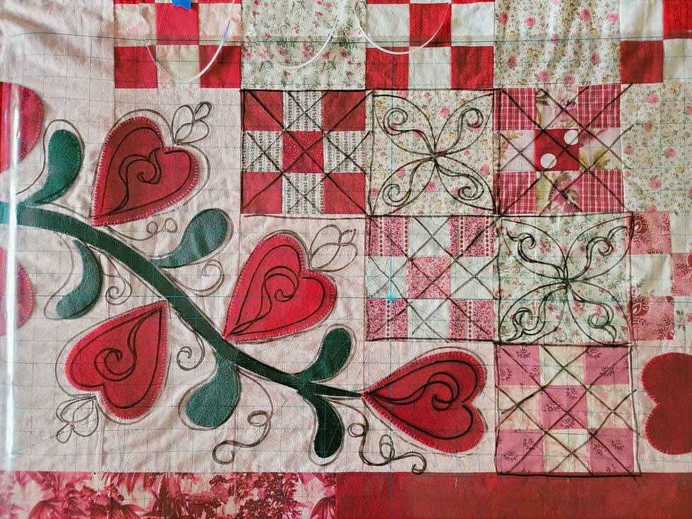 Patchwork quilt with red hearts and green vine motifs on a gridded fabric background, in pink, cream, and floral patterns.