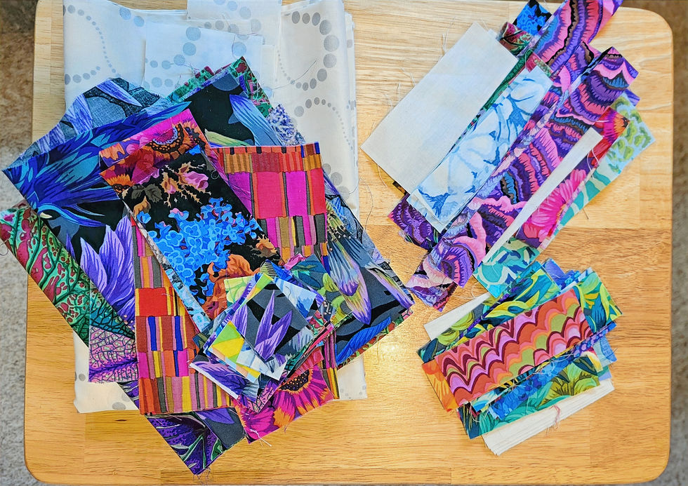 Colorful quilt fabric swatches and strips layered on a wooden table, showing bold floral, striped, and abstract patterns.