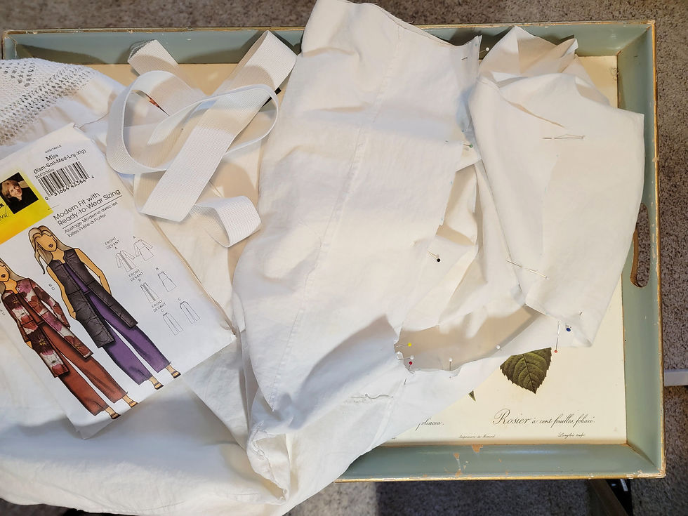 White garment pieces pinned in a tray, with a sewing pattern packet and measuring tape; calm craft workspace scene
