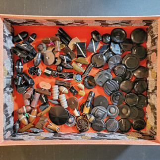A box with a red base filled with mostly black buttons