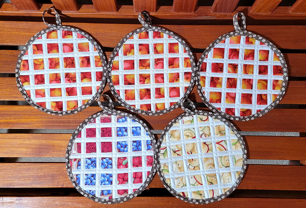 Five round quilted fruit-patterned potholders hang on a wooden slatted bench, showing apples, berries and pears.