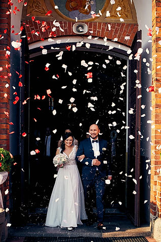Nowożeńcy wychodzący z kościoła po uroczystości ślubu. Na pierwszym planie widoczne confetti. Zdjęcie ślubne autor-Piotr Urban-fotograf ślubny.