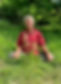 John Leah sitting in the grass, smiling and looking slightly off camera. He's wearing a red shirt with symbols on it.