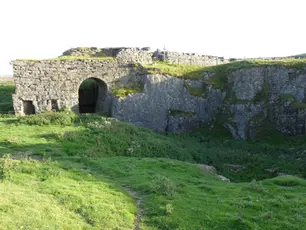 Ancient stone ruins with an archway sit atop a grassy cliff. The background features a clear sky, enhancing the serene atmosphere.