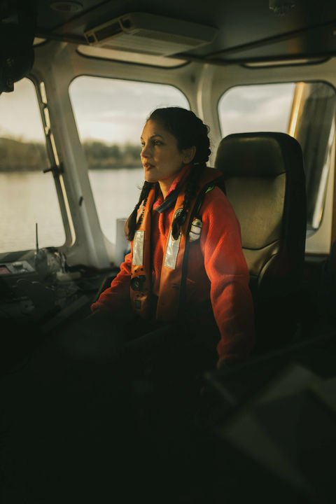 Foss Maritime crew member in orange life vest piloting tugboat from wheelhouse on Columbia River near Portland Oregon
