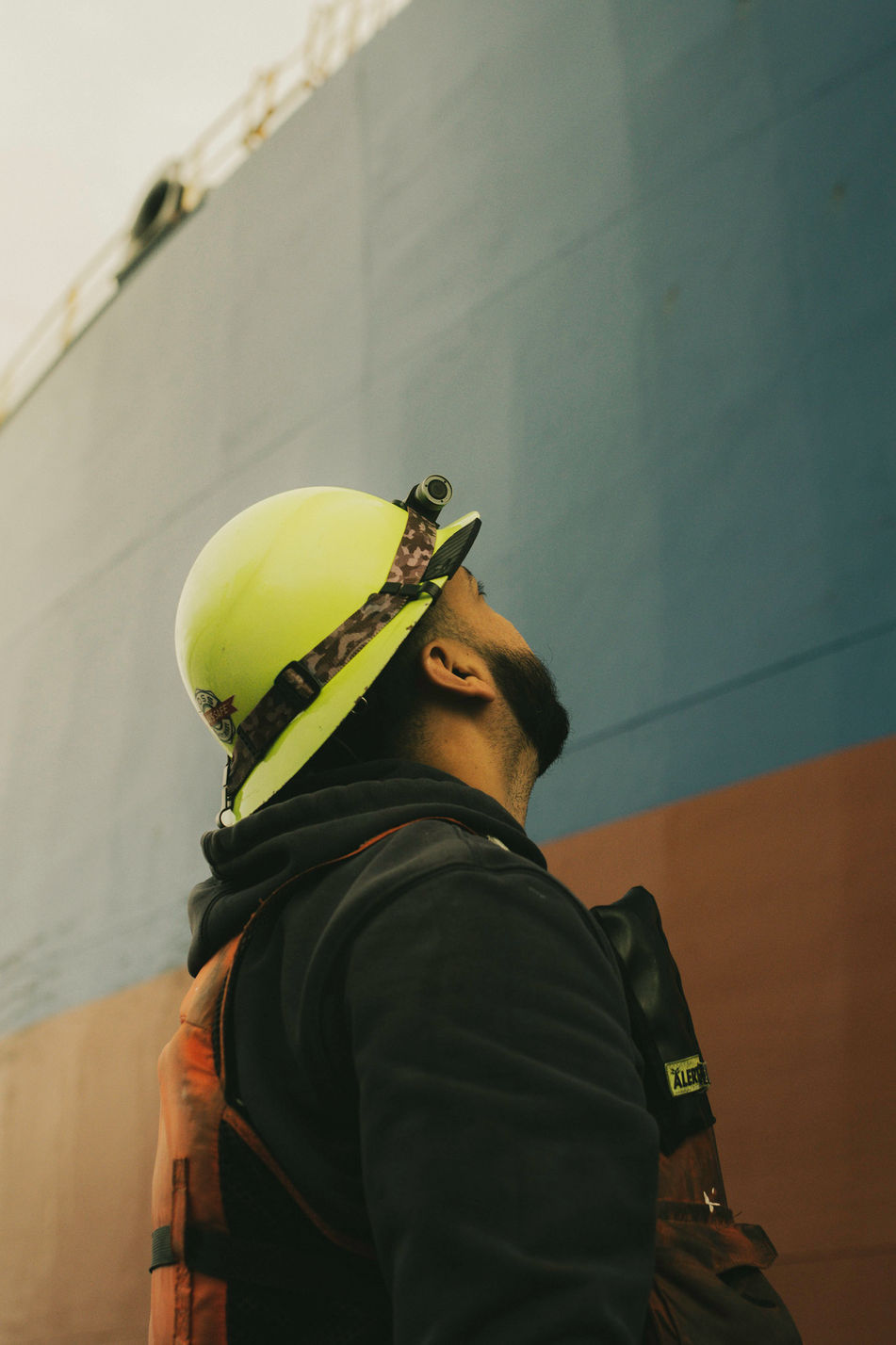 Foss Maritime crew member in yellow safety helmet looking up while waiting for line from bulk carrier Hiroshima Star on Columbia River near Portland Oregon
