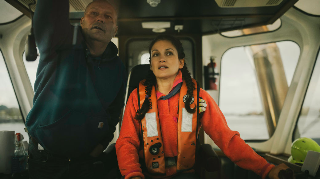 Tugboat captain and crew member in orange safety vest working in wheelhouse during Columbia River operations in Oregon