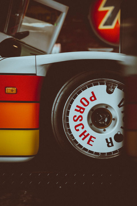 Close-up of white Porsche 962 racing wheel with red Victor lettering and rainbow stripe bodywork at Pelican Parts Torrance California
