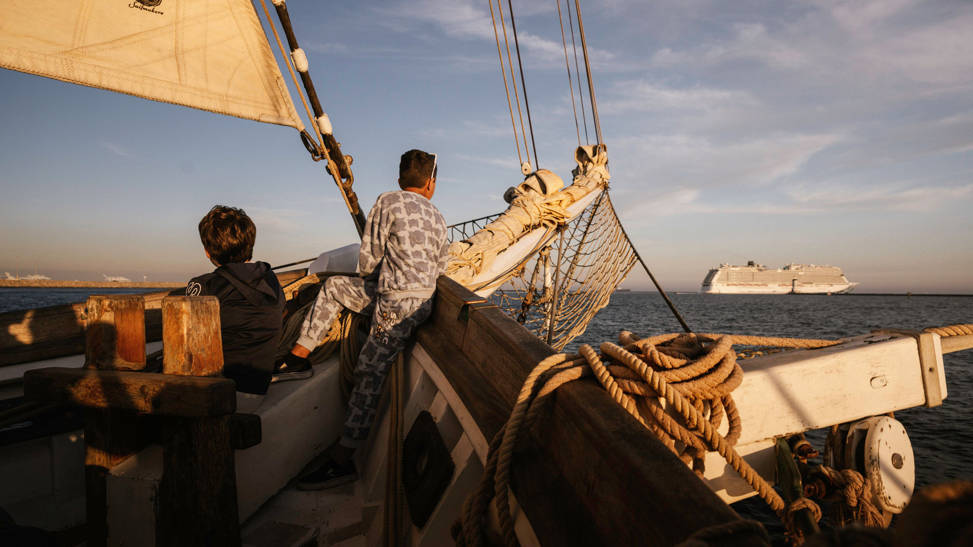 Young passengers on deck of tall ship brigantine Irving Johnson with sails and rigging visible, cruise ship in background at Los Angeles Harbor