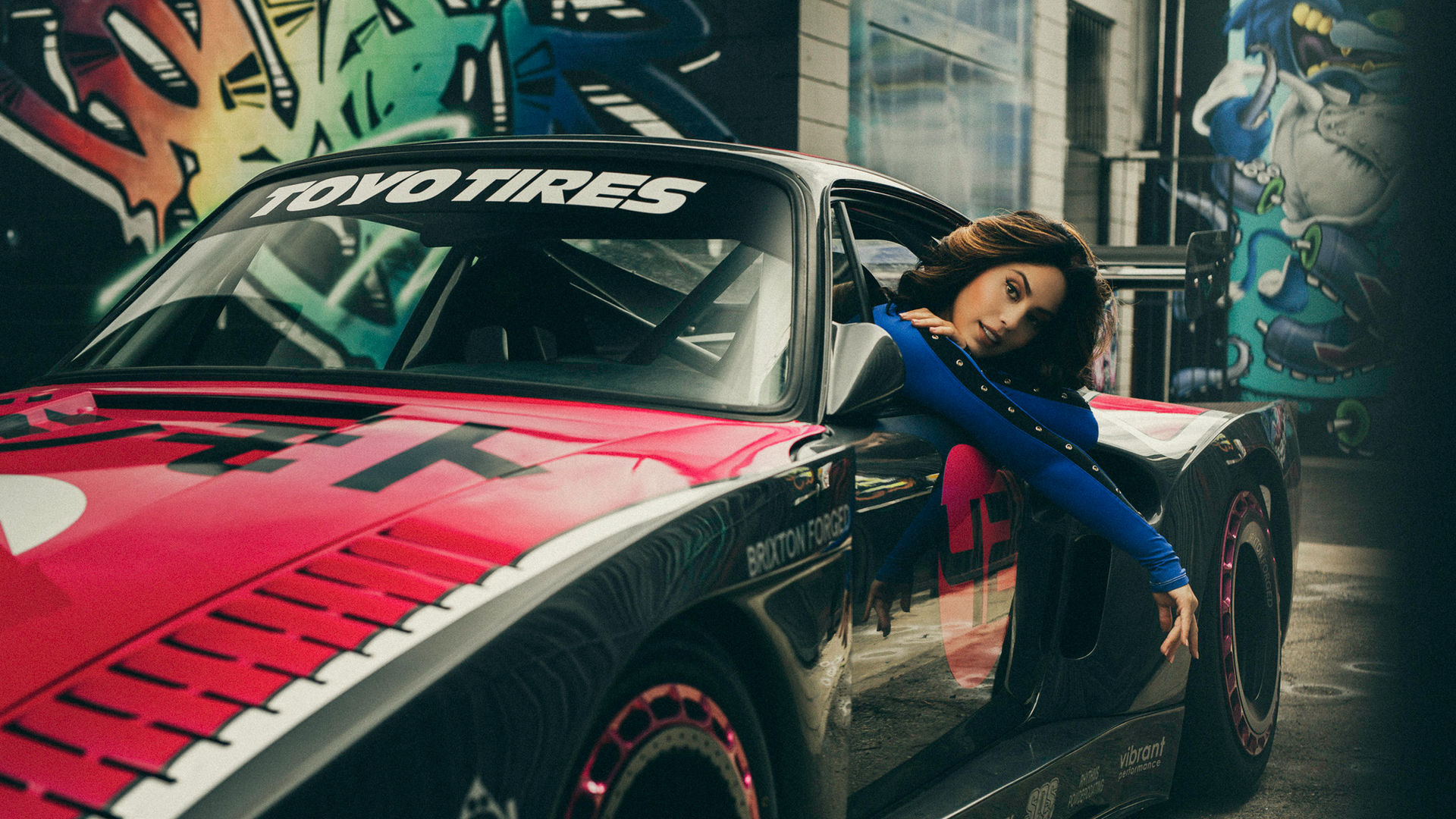 Model Samantha Kumiko in blue outfit leaning against red and black Bisimoto Porsche 935 with Toyo Tires branding in Los Angeles
