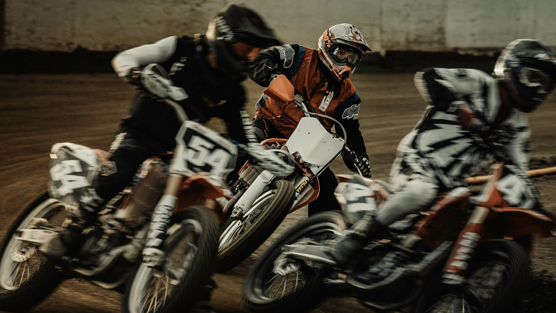 Multiple flat track motorcycles with motion blur racing in tight pack at Perris Speedway California dirt track
