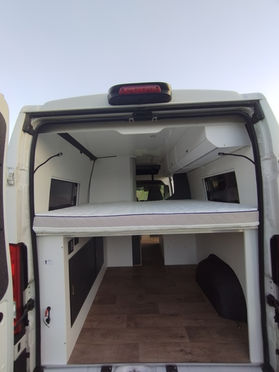 Ein moderner Campervan. Der Van ist weiß mit schwarzen Akzenten und bietet Platz für mehrere Personen, ideal für Camping und Roadtrips.