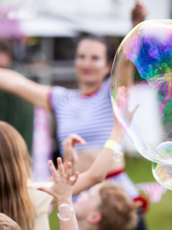 Iridescent giant bubble floating with young children's hands reaching towards it
