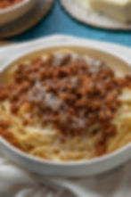 Spaghetti topped with rich Bolognese sauce and grated cheese in a white bowl. Blue background and a partial view of grated cheese nearby.