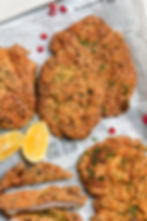 Breaded schnitzels on parchment-lined tray with lemon wedges and pomegranate seeds. Parsley garnishes add a fresh touch.