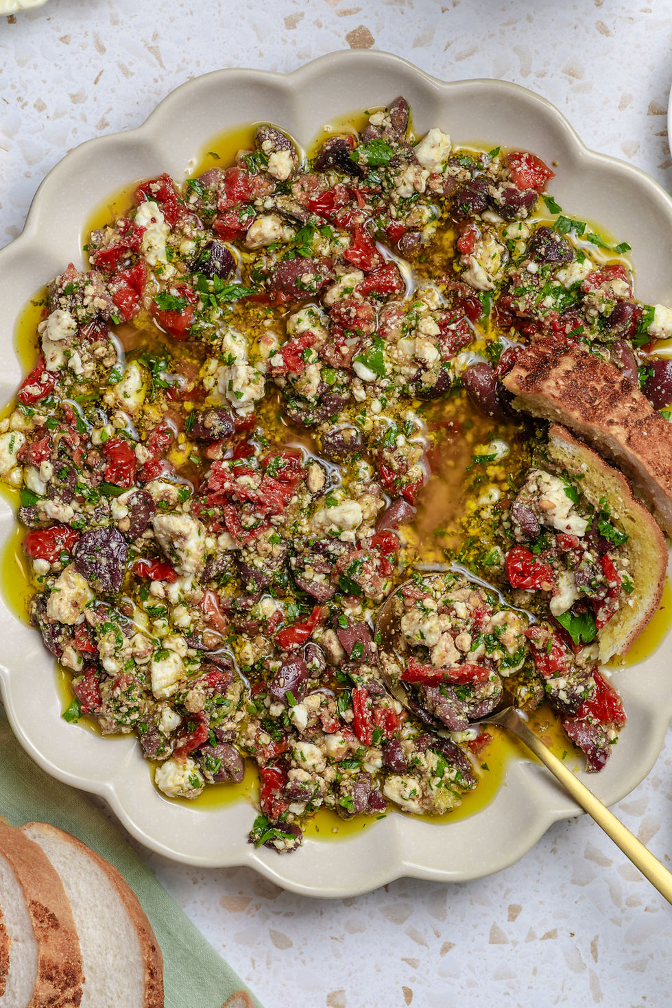 Dish with feta, olives, herbs, and olive oil on a textured plate. Bread slices on the side. Bright, colorful, appetizing presentation. Greek Salad Bread Dipping OIl
