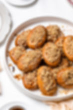Cookies topped with crushed nuts are arranged on a white plate. The background is white, enhancing the warm, golden-brown hues.