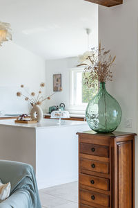a green vase with dried flowers in it sits on a wooden dresser