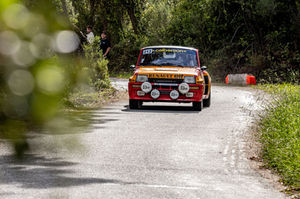 a red and yellow renault car is driving down a road