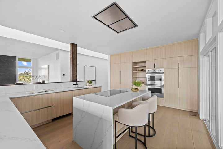 Contemporary kitchen with minimalist design, quartz waterfall island, light oak cabinetry, and seamless open flow. Faver Drive Remodel.